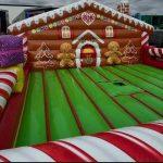 Inflatable gingerbread house bounce castle with red and white striped base and green bounce floor for children's entertainment.