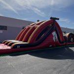 Red inflatable pirate-themed obstacle course setup on asphalt with industrial building in background.