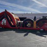 Red and black inflatable pirate-themed obstacle course with tunnels and climbing elements on outdoor pavement.