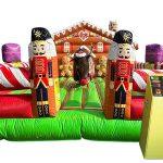 Colorful inflatable bounce house with reindeer theme, red walls, green base, and purple turrets for children's entertainment.